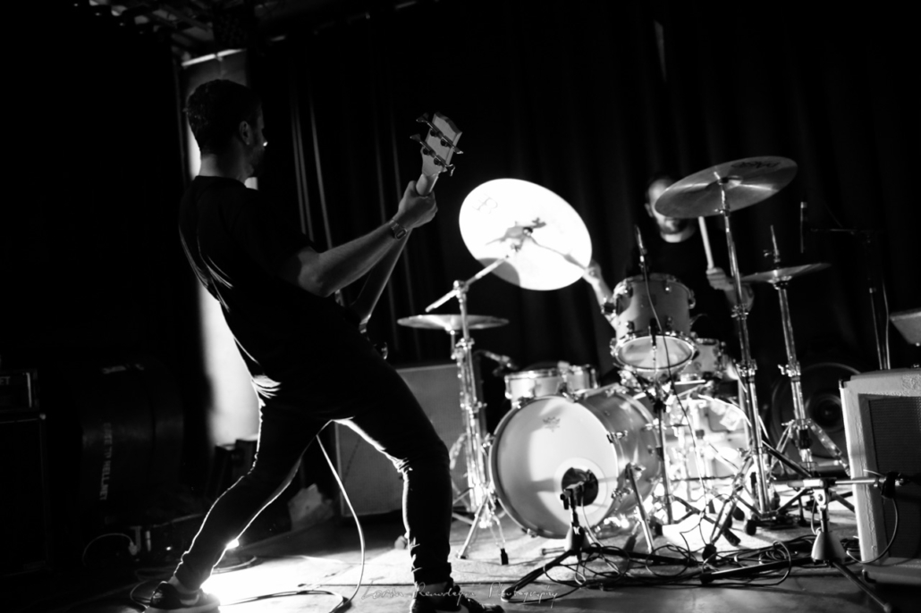 Backlit guitarist with back to audience and lighted drumkit